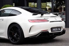 the rear end of a white sports car parked in front of a building with black rims