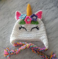 a crocheted unicorn hat with flowers on it's head is laying on a marble surface