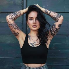 a woman with tattoos on her arms and shoulder posing for a photo in front of a wooden wall