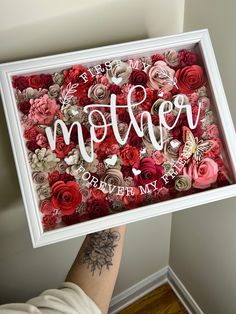 a person holding up a framed sign with flowers on it that says mother and the words,