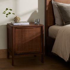 a bed with a brown headboard next to a night stand and a vase on top of it