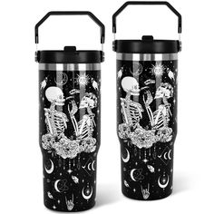 two black tumblers with skeletons on them and stars in the sky, one is holding a