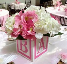 pink and white flowers are in a square vase on a table with tables cloths