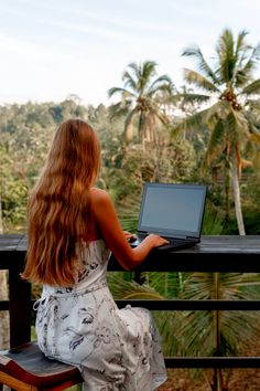 a woman sitting at a table with a laptop on her lap looking out over the jungle