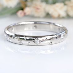 a white gold wedding band with stars and diamonds on the side, in front of flowers