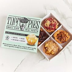 four boxes of tiny pies sitting on top of a white marble countertop next to each other