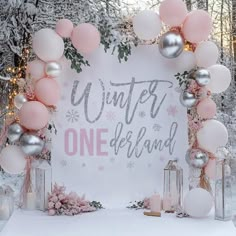 a winter onederland sign surrounded by balloons and candles in front of snow - covered trees