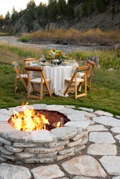 a fire pit in the middle of a field with chairs around it and a table set for four