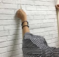 a person holding onto a white brick wall with a black and white checkered shirt on