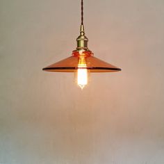 a light hanging from a ceiling with a white wall behind it and a brown cord on the end