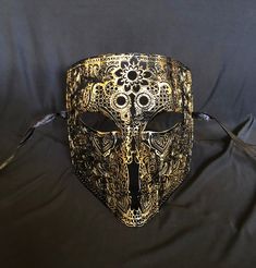 This men's Venetian masquerade mask is made of a lightweight metal and is hand painted in gold and black. The abstract paint job gives the mask a unique look. Stand out at your next costume or masquerade party with this awesome mask! Mask has some flexibility and come with black silk ribbon ties attached. Mask size 6"W x 7"H. Mask color gold/black Gold Masquerade Mask For Carnival Cosplay, Gold Costume Masks For Halloween, Gothic Masks For Mardi Gras Theater, Venetian Gold Masquerade Mask For Halloween, Gold Venetian Masquerade Mask For Halloween, Gothic Masks For Theater And Mardi Gras, Gold Venetian Mask For Halloween, Gold Fantasy Festival Masks And Prosthetics, Gothic Gold Masks And Prosthetics For Costume