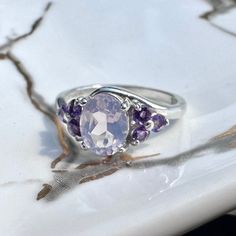 The Laura Ring is elegant for both everyday where and special occasions.  1 - 8x6mm Lavender Moon Quartz 6 - 2.5mm Amethyst Sterling Silver  10% of proceeds will be donated to benefit CAST LA to combat human trafficking. Purple Amethyst Oval Cabochon Ring, Lavender Gemstone Promise Ring, Lavender Gemstone Accent Promise Rings, Lavender Promise Rings With Gemstone Accents, Lavender Crystal Birthstone Ring For Anniversary, Fine Jewelry Lavender Amethyst Birthstone Ring, Lavender Amethyst Ring With Gemstone Accents For Promise, Lavender Amethyst Ring With Gemstone Accents As Gift, Lavender Amethyst Ring With Gemstone Accents