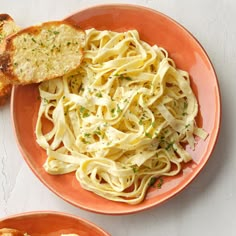 two orange plates with pasta and bread on them, one has parmesan cheese