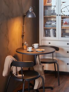 a small table with two chairs next to it and a book shelf in the background