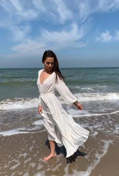 a woman in white dress walking on the beach