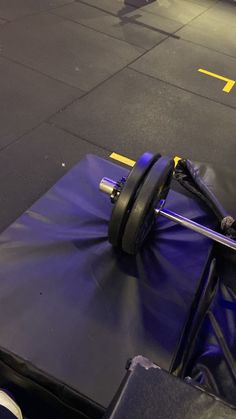 a barbell sits on top of a blue bag in a gym floor with yellow lines