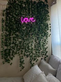 a bed with white pillows and a pink neon sign on the wall above it that says love