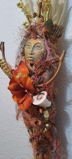 a mask with feathers and flowers on it's head is hanging against a wall