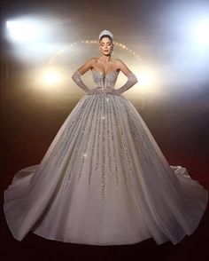 a woman in a ball gown with long sleeves and beading on her shoulders, standing in front of spotlights