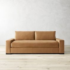 a tan couch sitting on top of a wooden floor next to a white wall in an empty room