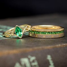 two wedding rings with green stones on top of each other, sitting on a book