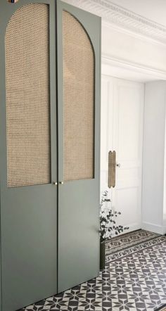 an open door in a room with black and white floor tiles on the floor, and a plant next to it