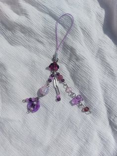 a purple necklace with beads and charms hanging from it's side on a white cloth