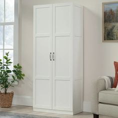 a white armoire in a living room next to a couch and potted plant