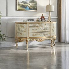 a white and gold dresser sitting in a living room next to a painting on the wall