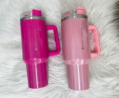 two pink travel mugs sitting next to each other on a white fur covered floor