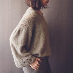 a woman standing in front of a wall with her back turned to the camera, wearing a sweater and pants