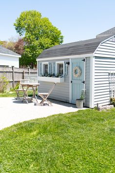 a small white shed sitting on top of a lush green field next to a picnic table