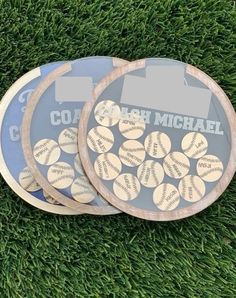 three baseball coasters sitting on top of green grass with the name coach michael written on them