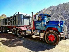 a blue dump truck parked on the side of a dirt road next to a mountain