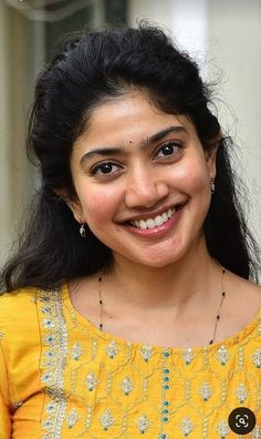 a smiling woman in a yellow top and gold necklace with a smile on her face