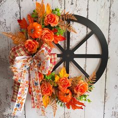 an orange wreath with flowers and leaves on a wheel hanger against a white wooden wall