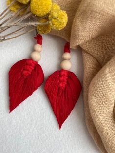 two red tasseled earrings with wooden beads and wood beads on them, sitting next to some yellow flowers