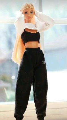 a barbie doll with blonde hair wearing black sweatpants and cropped white top standing in front of a window