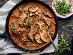 a skillet filled with meat and mushrooms on top of a wooden table