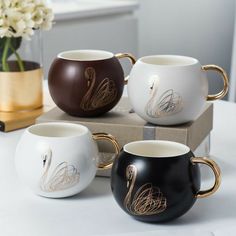 three coffee mugs sitting on top of a box next to a vase with flowers