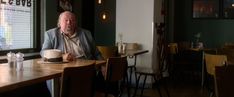 an older man sitting at a table with a hat on his head in a restaurant