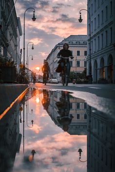 a person riding a bike down a street next to tall buildings and water puddles