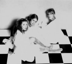 black and white photograph of three women sitting on a checkered floor with their arms around each other