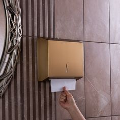 a hand holding a paper towel dispenser in front of a wall mounted toilet paper dispenser