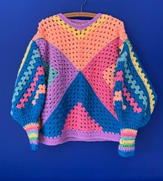 a colorful crocheted sweater hanging on a blue wall