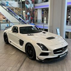 a white mercedes sls parked in front of a staircase at a mall or shopping center