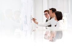 three people are looking at a whiteboard while one person is writing on the board