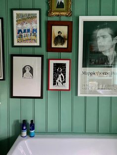 a bathroom with green walls and pictures on the wall above the bathtub in front of it