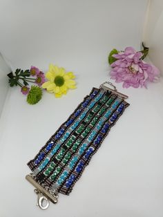 a blue and black beaded bracelet next to flowers on a white surface with metal clasp