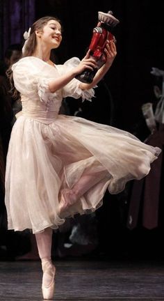 a ballerina in a white dress is performing on stage with her arms outstretched and legs spread out